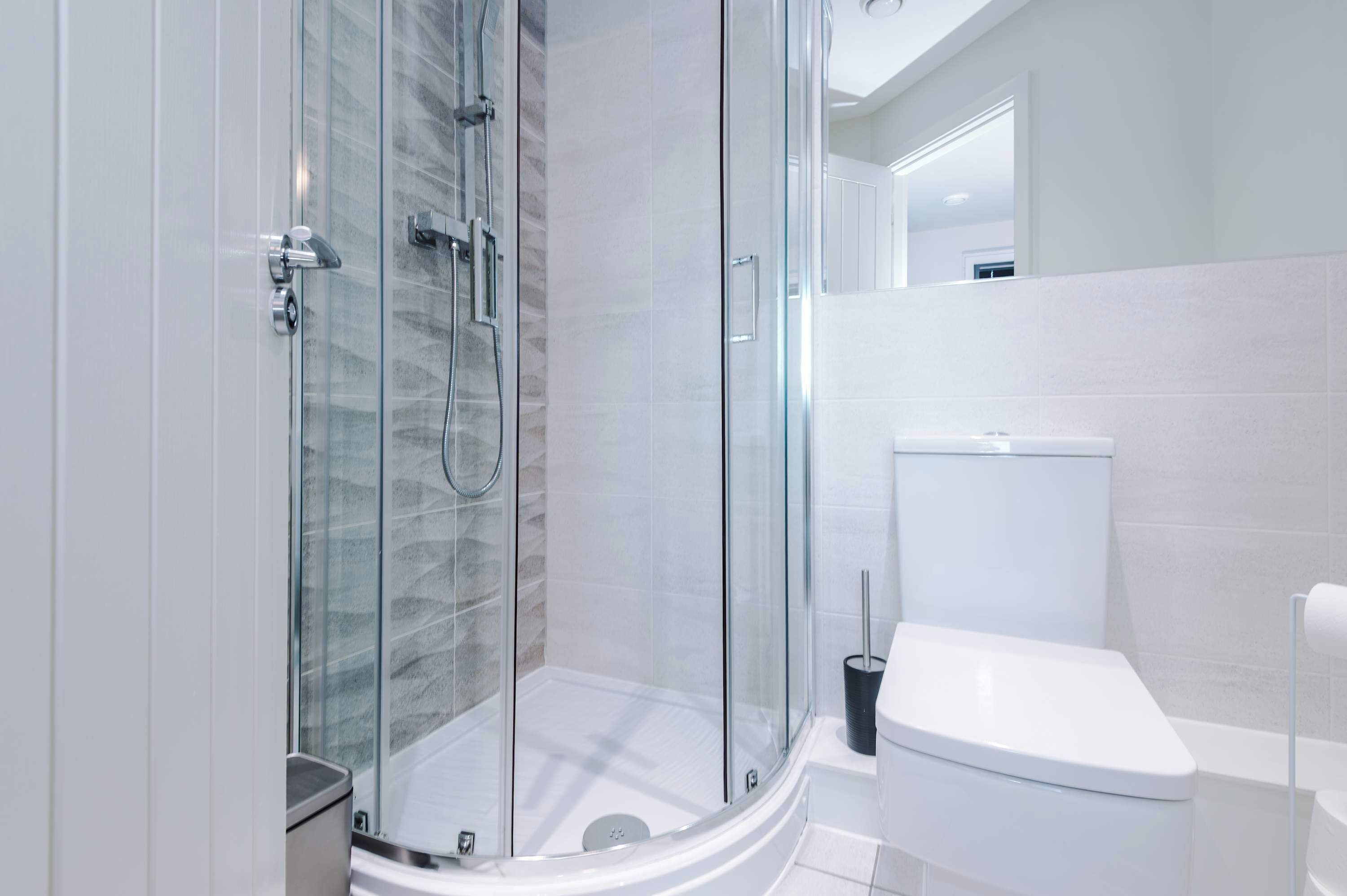 Une salle de bain moderne avec une douche à parois de verre, des toilettes blanches et un miroir au-dessus du lavabo.