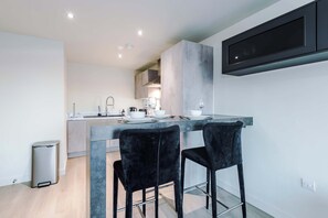 A modern kitchen with a central island, two black bar stools, and a built-in TV.