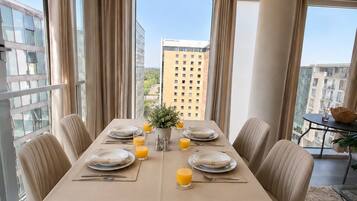 A dining area with a table set for four, large windows, and a view of city buildings.