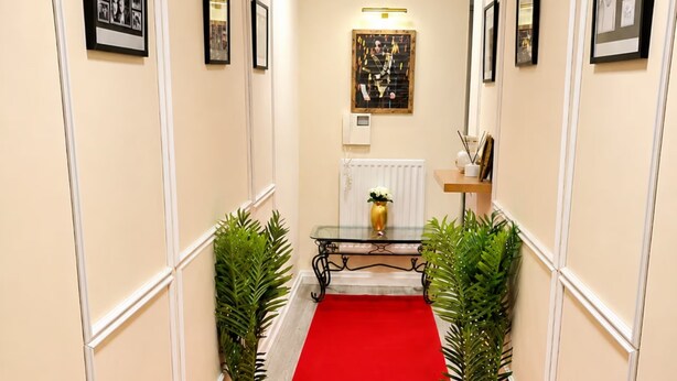 A hallway with a red carpet, potted plants, framed pictures, and a table with a vase. - VIP-Themed Luxury Apartment Central Milton Keynes City Views & Pool Table (Milton Keynes)