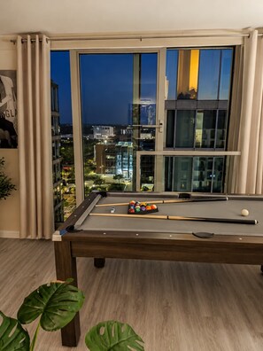 Ein Billardtisch in einem Raum mit einem großen Fenster mit Blick auf eine nächtliche Skyline.