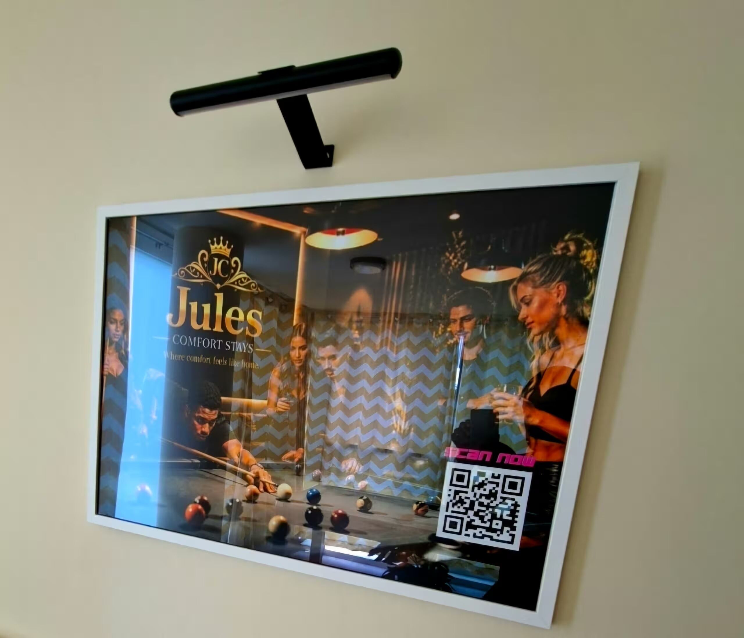 A framed photo of a billiards table with people playing, a QR code, and the text 'Jules COMFORT STAYS.'
