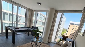 A spacious living room with a pool table, a sofa, a coffee table, and a large window offering a city view. - VIP-Themed Luxury Apartment Central Milton Keynes City Views & Pool Table (Milton Keynes)