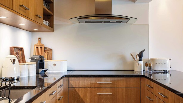 A modern kitchen with wooden cabinets, a stainless steel range hood, and a black countertop. - Central Verbier | Sleeps 6 | Near Ski Lifts (Val de Bagnes)