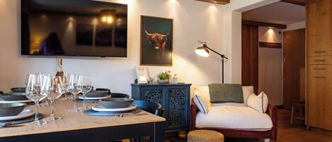 Un comedor con una mesa de madera lista para una comida, un sofá, una silla y un televisor montado en la pared.