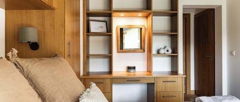 A bedroom with a wooden desk, a bed, a nightstand, a mirror, and a wall-mounted lamp.