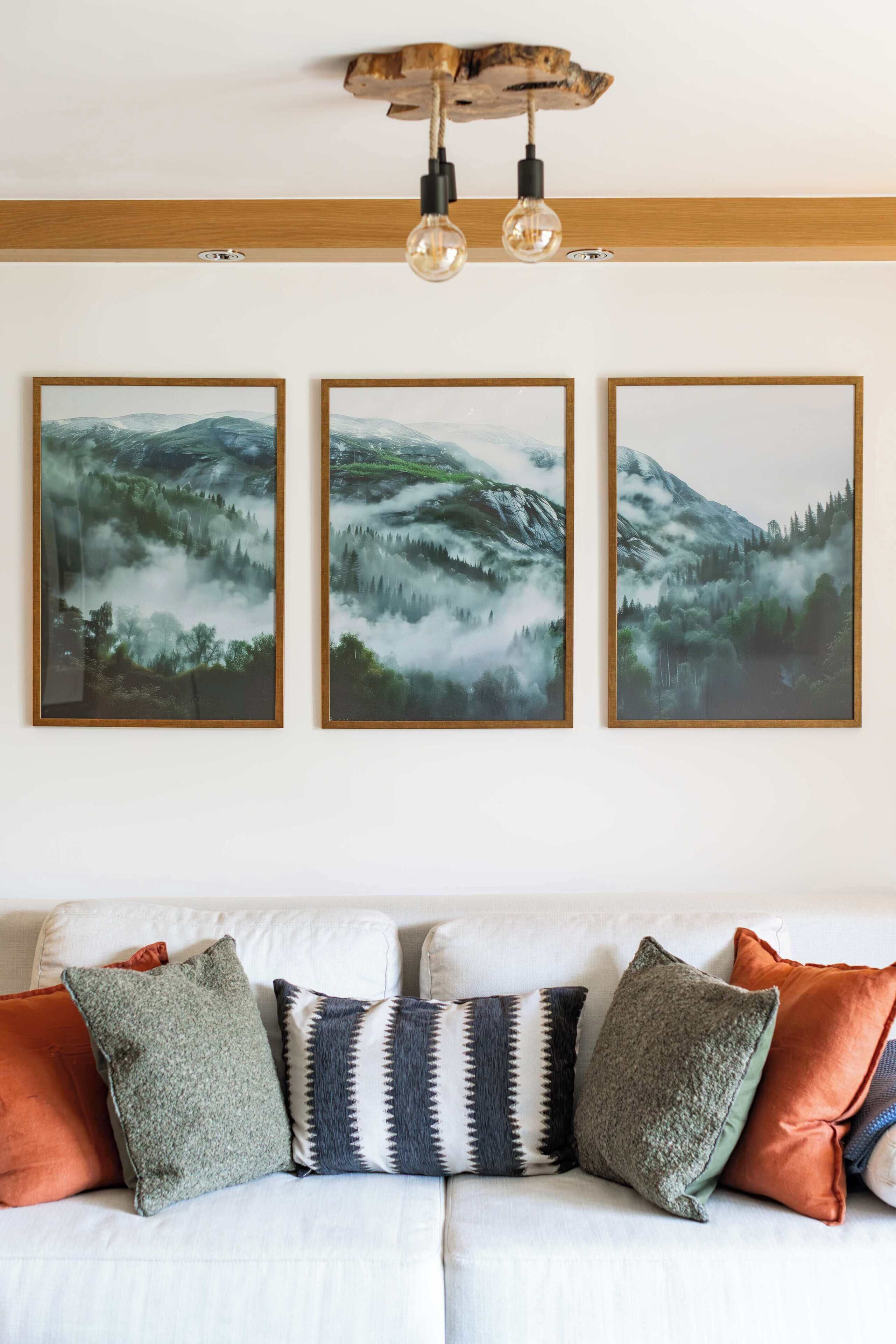 Une pièce avec un plafond en bois, un luminaire et trois tableaux représentant des paysages, encadrés et accrochés au mur.