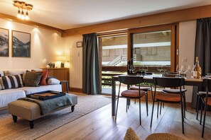 Ein modernes Wohnzimmer mit einer Couch, Hocker und einem Essbereich mit Stühlen und Tisch, gedeckt für eine Mahlzeit.