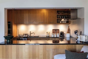 A modern kitchen with wooden cabinets, a black countertop, and stainless steel appliances. - Central Verbier | Sleeps 6 | Near Ski Lifts (Val de Bagnes)