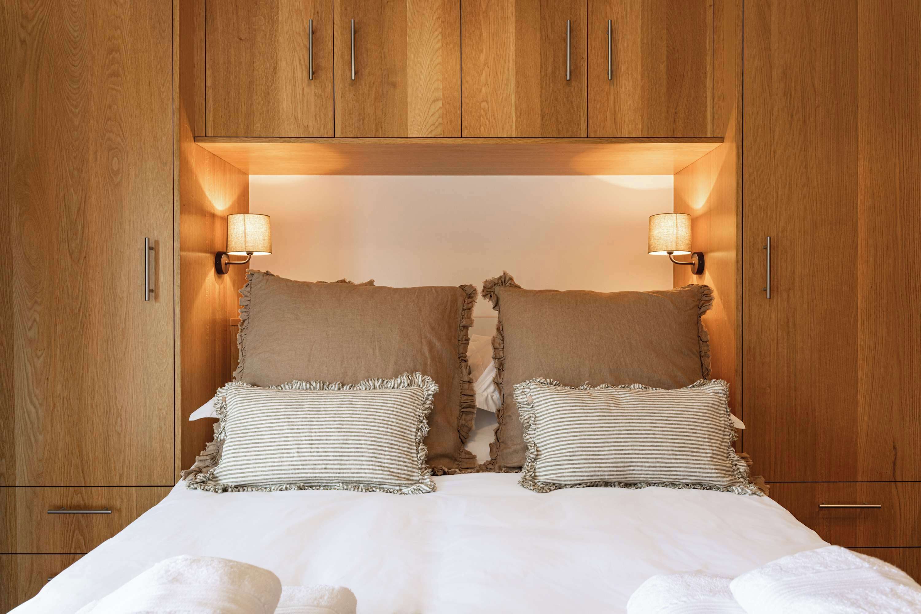 A bedroom with a wooden wardrobe, two bedside lamps, and a bed with striped pillows.
