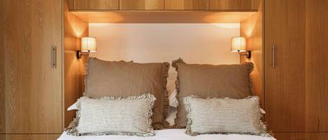 A bedroom with a wooden wardrobe, two bedside lamps, and a bed with striped pillows.