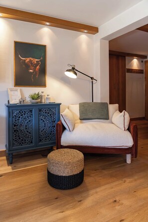 Ein gemütliches Wohnzimmer mit einer Couch, einem runden Hocker, einem dekorativen Schrank, einer Stehlampe und einem gerahmten Kunstwerk an der Wand.