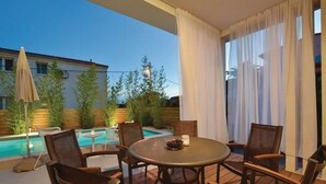 Un espace aménagé au bord de la piscine, avec une table ronde et des chaises, une piscine, et un bâtiment en arrière-plan.