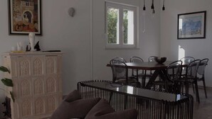 Un coin repas avec une table et des chaises, un buffet blanc orné de panneaux décoratifs et une fenêtre donnant sur un paysage verdoyant.