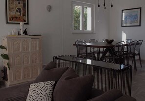 A dining area with a table and chairs, a white cabinet with decorative panels, and a window with a view of greenery. - Villa Bamboo - Green villa with heated pool (Duće)