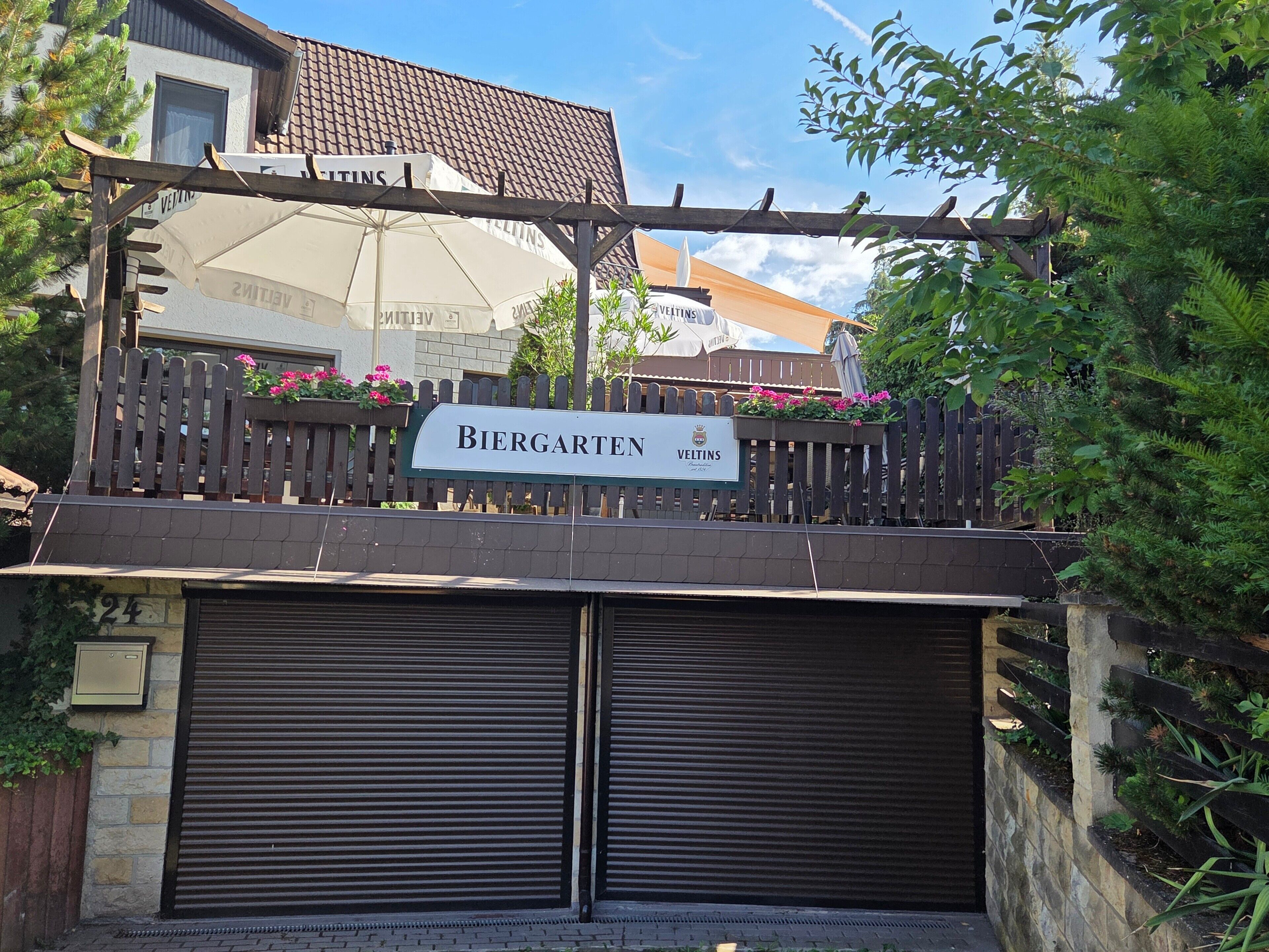 Ein begrenzter Eingang mit einem Schild, auf dem 'Biergarten VELTINS' steht.