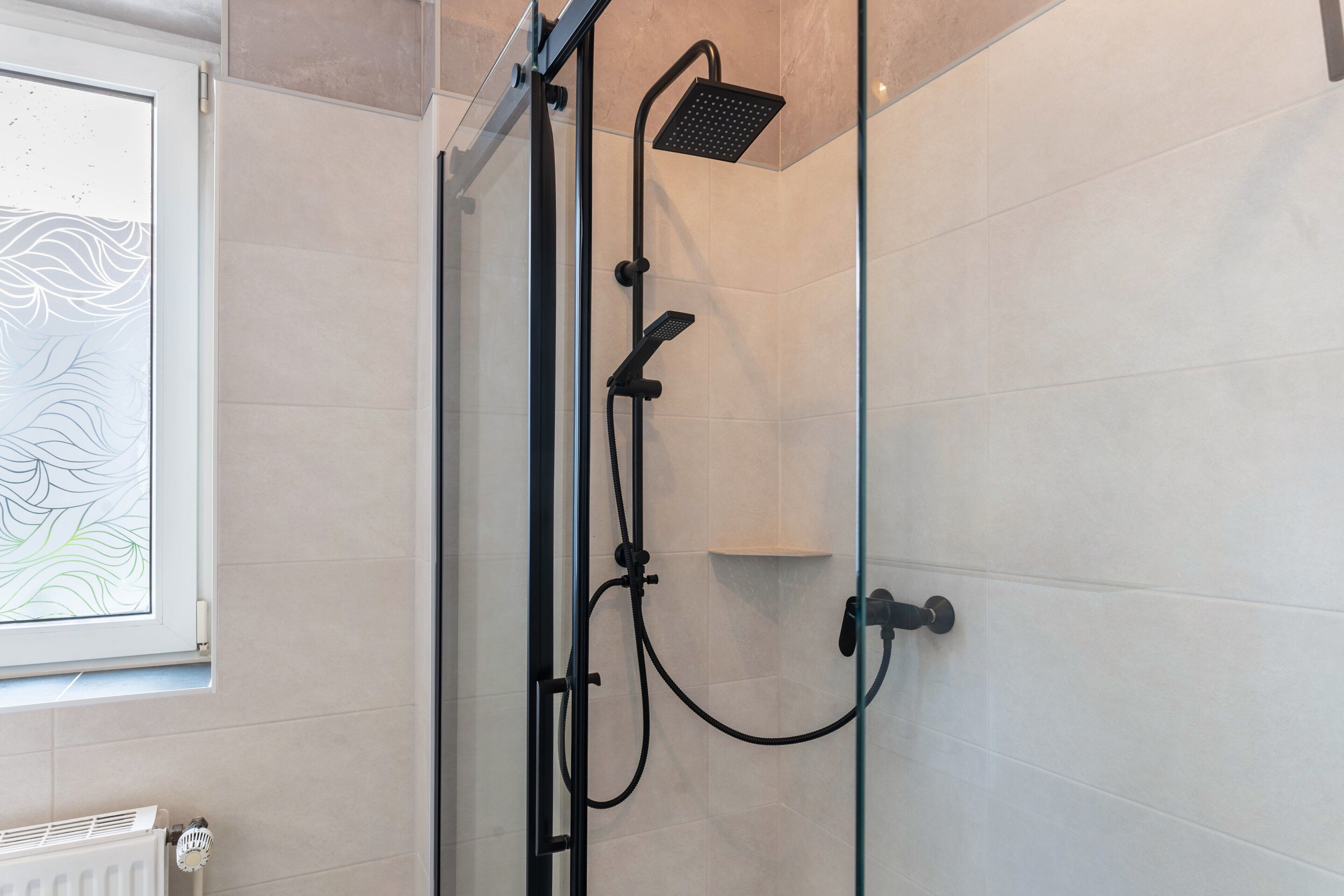 A glass-enclosed shower with a handheld showerhead and a fixed showerhead.