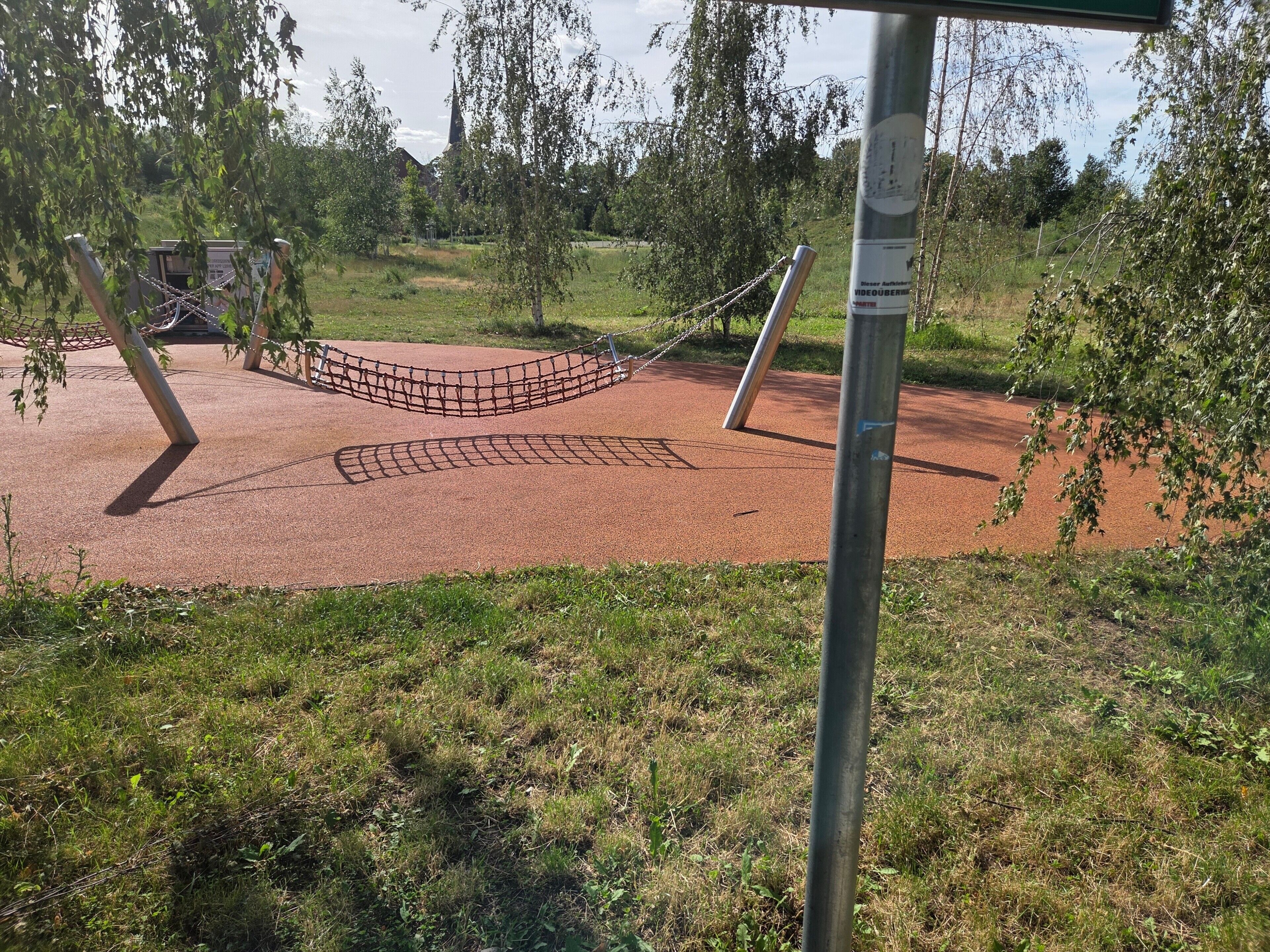 Ein Spielplatz mit einer Seilnetzanlage, einem Metallpfosten und einer roten Oberfläche.