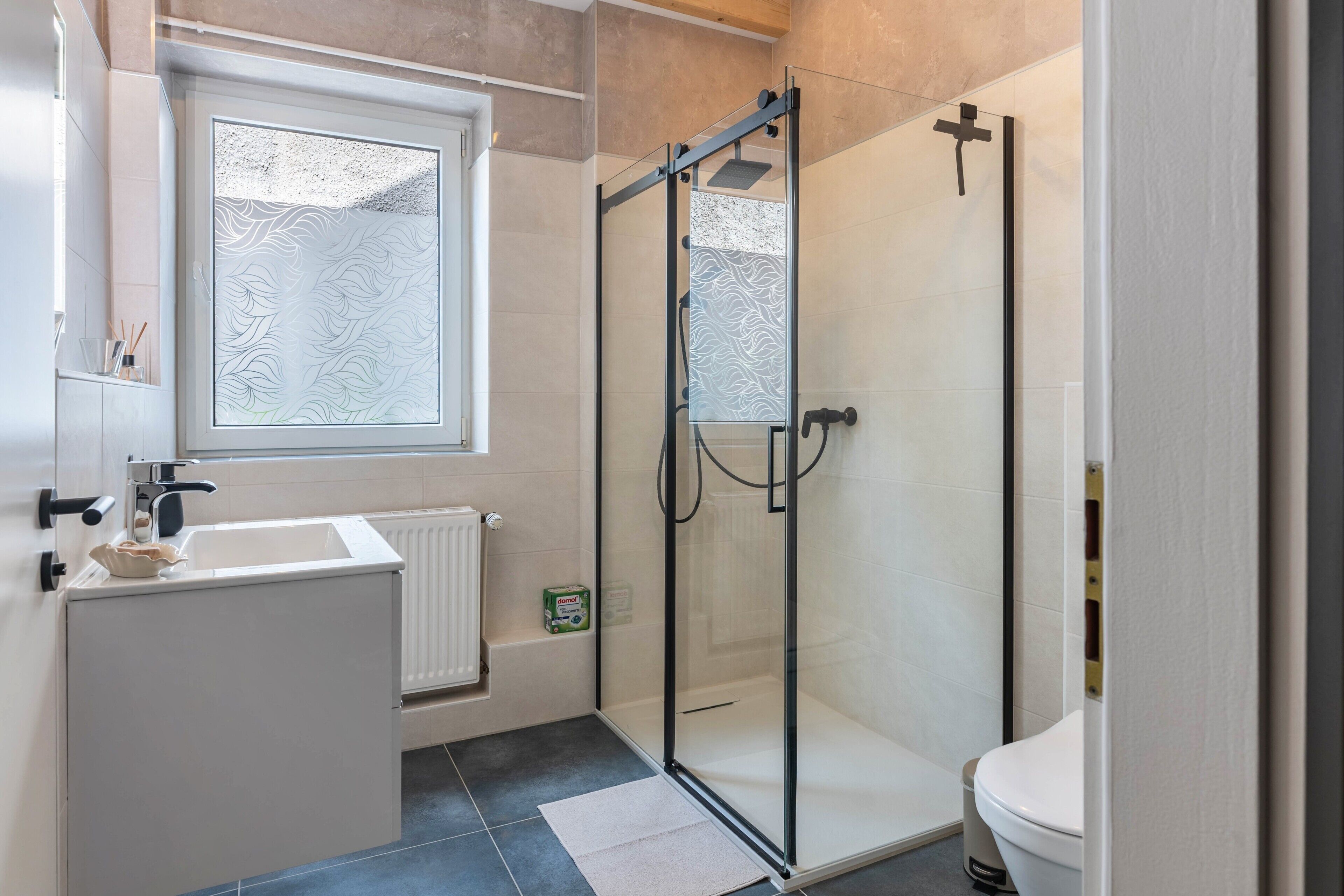 A modern bathroom with a glass shower enclosure, a white sink, and a toilet.