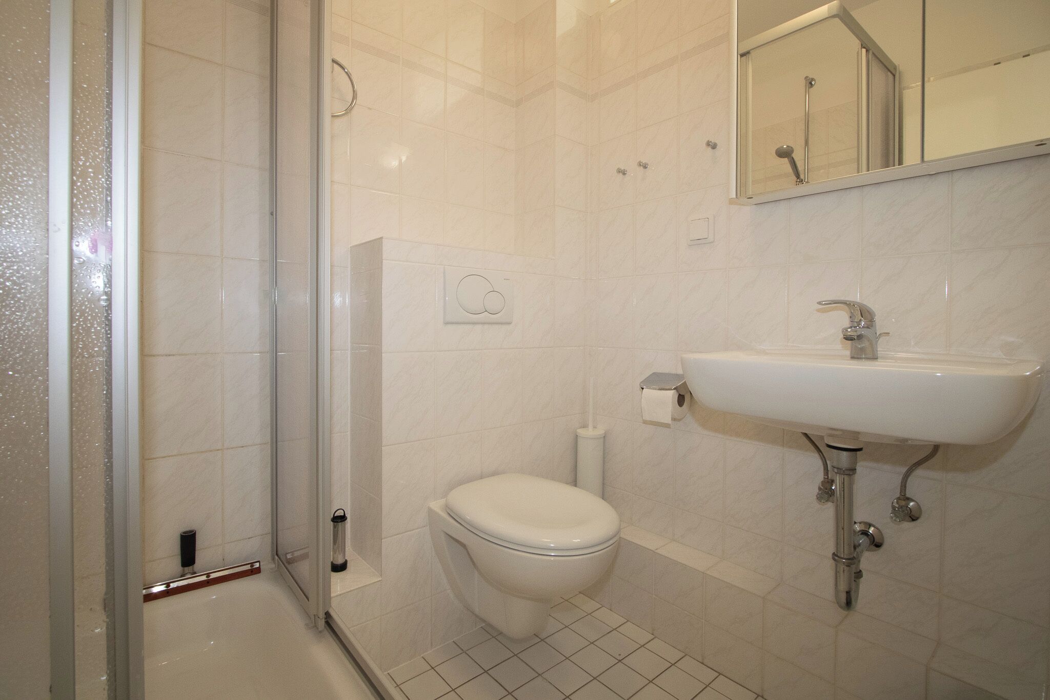 Un baño con cabina de ducha de vidrio, inodoro y lavamanos con espejo.