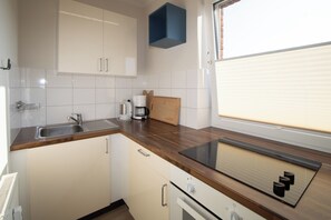 A kitchen with a built-in stove, a sink, and a window with blinds. - Beachfront vacation rental in Hörnum, right next to the golf course. (Hörnum (Sylt))