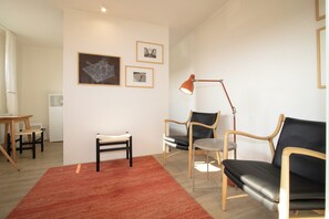 Ein Wohnzimmer mit rotem Teppich, zwei schwarzen Ledersofas, einem Holztisch, einem weißen Sessel und einem Schreibtisch mit Lampe.