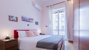 Ein Schlafzimmer mit Bett, Nachttischen, einem Fenster mit Vorhängen und Wandbildern.