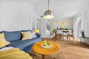 Een moderne woonkamer met een blauwe bank, een ronde houten salontafel en een eethoek met een witte tafel en stoelen.