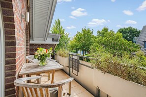 A balcony with a wooden table and chairs, a vase of flowers, and a view of greenery and buildings. - Nordstern Vacation Rental with Ocean Views and Two Balconies on Schönberg Beach (Schönberg (Holstein))