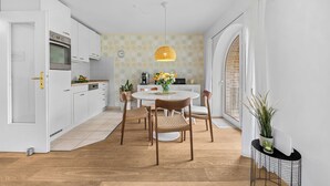 A modern kitchen with white cabinets, a built-in oven, and a dining area with a round table and chairs. - Nordstern Vacation Rental with Ocean Views and Two Balconies on Schönberg Beach (Schönberg (Holstein))