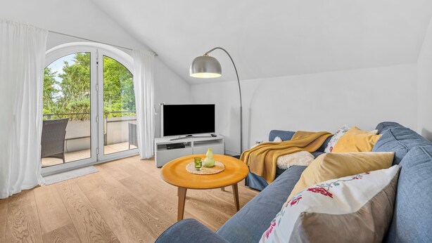 A modern living room with a sofa, a coffee table, a TV, and a balcony with curtains. - Nordstern Vacation Rental with Ocean Views and Two Balconies on Schönberg Beach (Schönberg (Holstein))