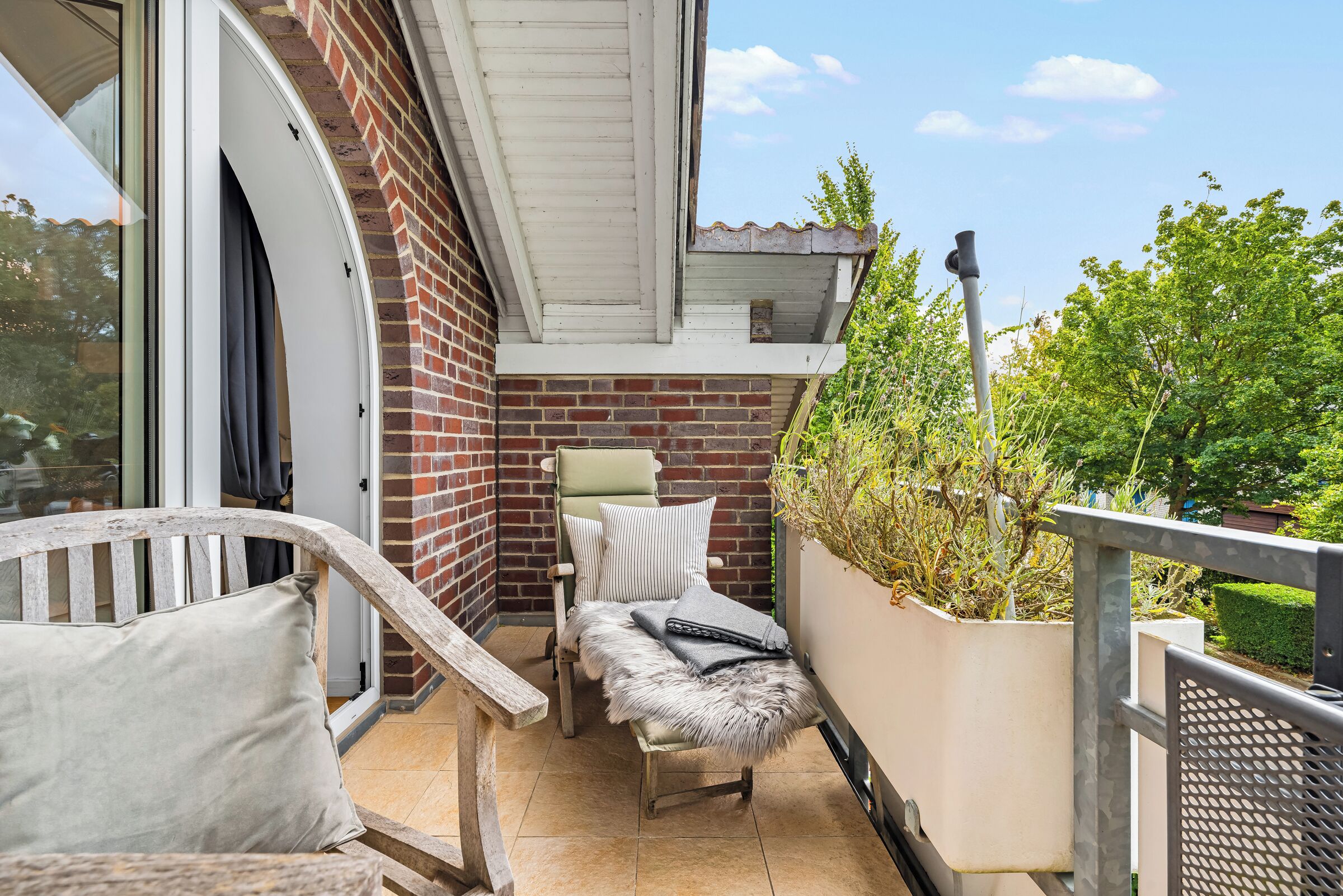 Ein Balkon mit Korbstuhl, gepolstertem Sitzplatz und einem Topfpflanzen.