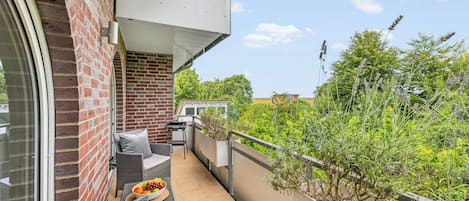 A balcony with outdoor furniture, a grill, and a view of greenery.