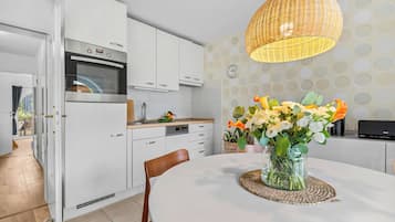A modern kitchen with white cabinetry, an oven, and a dining area with a round table and a vase of flowers.
