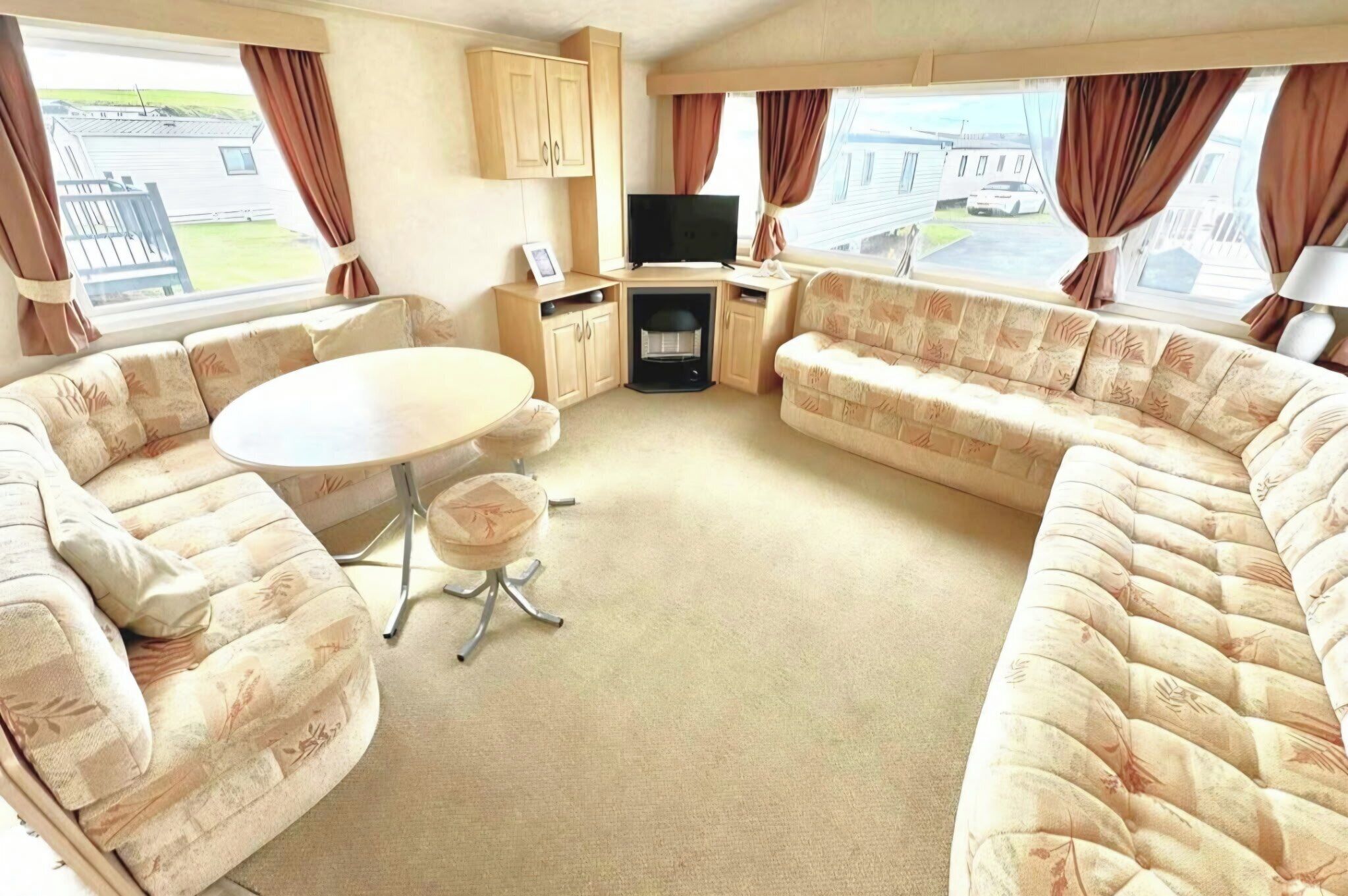 A caravan interior with a sofa set, a television, a table, and a fireplace.