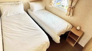 Una habitación pequeña y acogedora con dos camas, un aparador de madera, una mesita y una ventana con cortinas.