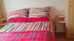 Ein Bett mit gestreiftem Überwurf und Kissen, zwei Nachttische und eine schlichte Wand.