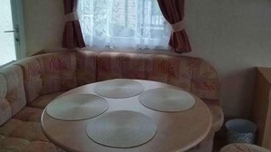 Ein Zimmer mit einer Couch, einem runden Tisch mit vier runden Untersetzern, einem Fenster mit Vorhängen und einem Mülleimer.