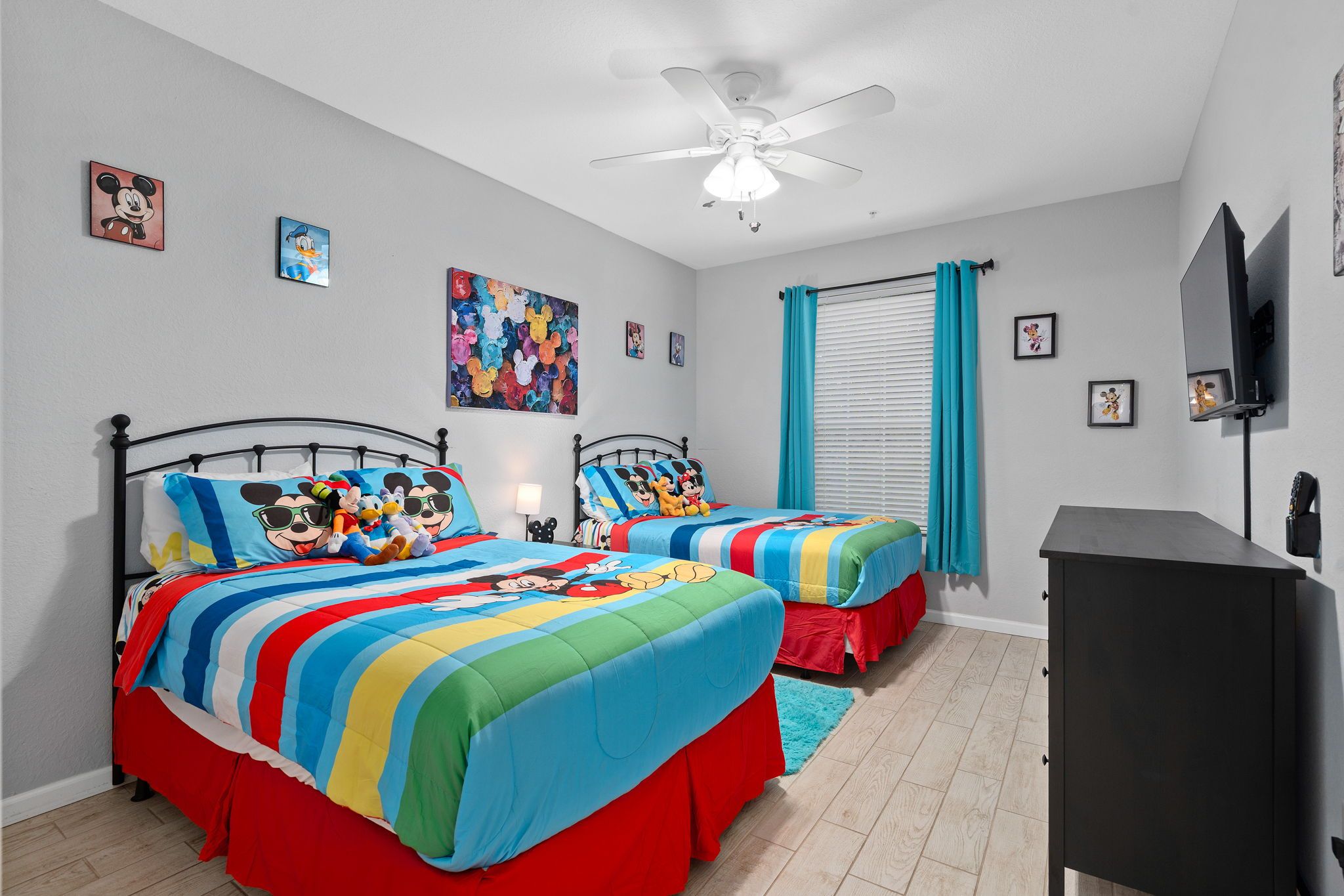 A bedroom with two beds, a ceiling fan, a TV, and a window with curtains.