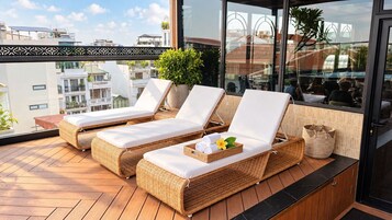 A balcony with wicker lounge chairs and a potted plant.