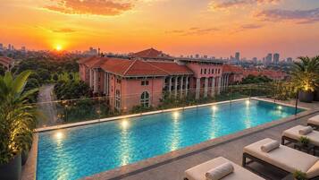 Una piscina con sillones de descanso, un edificio de techo rojo y vistas al atardecer.
