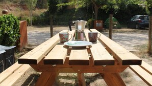 Uma mesa de piquenique de madeira com uma cafeteira, duas xícaras estampadas e um prato.