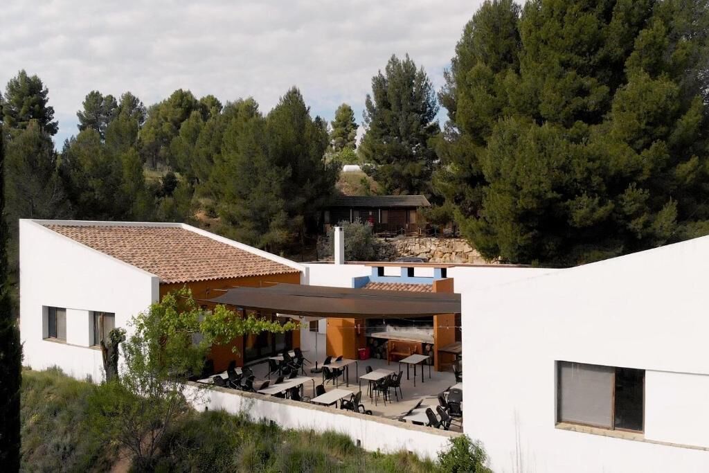 A modern building with a patio area, outdoor seating, and a view of a forested hill.
