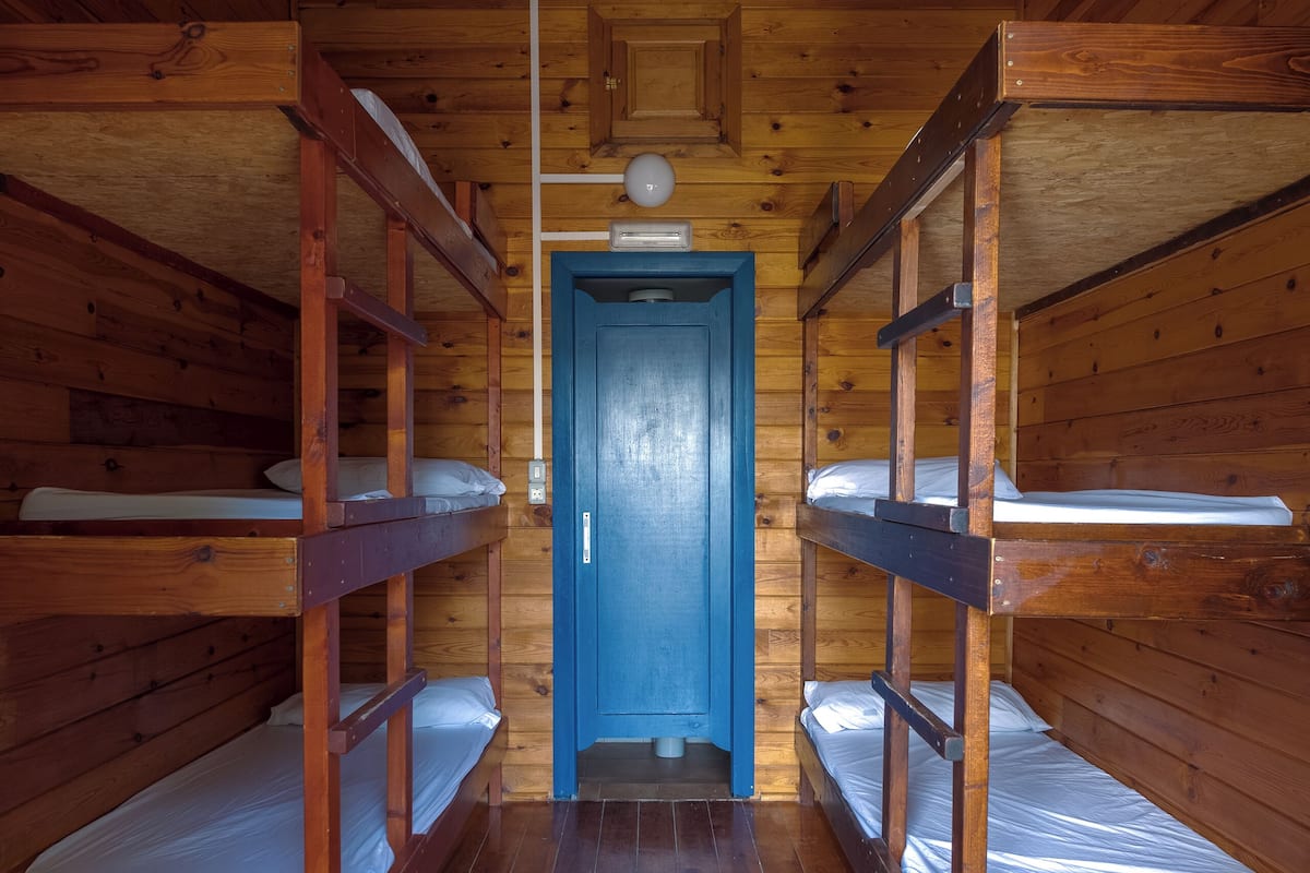 Una cabaña de madera con literas ubicadas en un pasillo que conduce a una puerta azul.