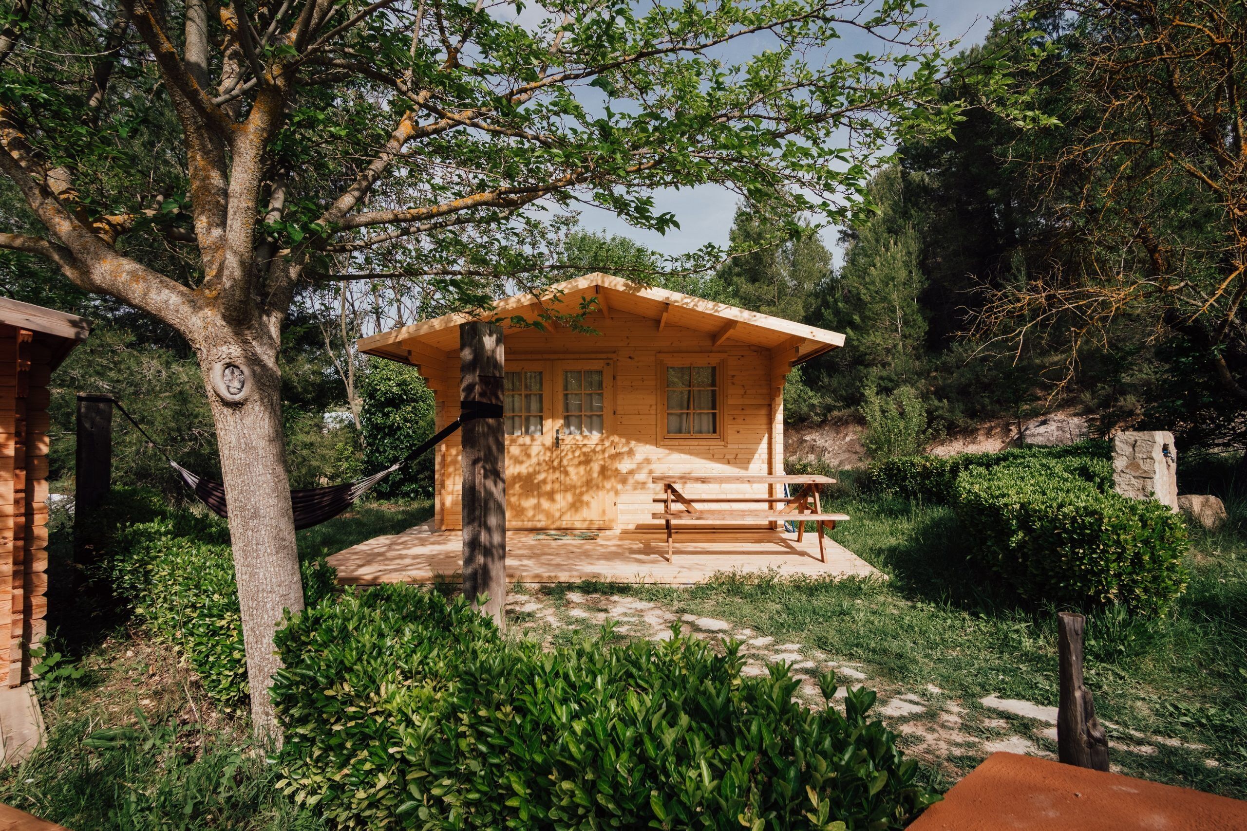 Una cabaña de madera con un porche, rodeada de abundante vegetación y árboles.