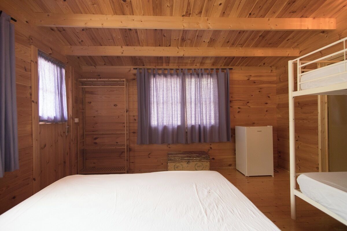 Een houten kamer met een stapelbed, een kleine koelkast en een raam met gordijnen.