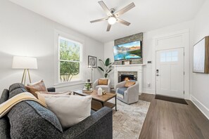 Ein Wohnzimmer mit einer Couch, Sesseln, einem Kamin, einem Fernseher und einem Deckenventilator.