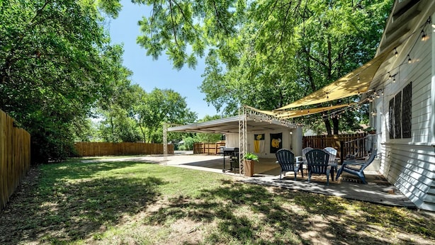 Ein Garten mit überdachter Terrasse, Sitzgelegenheiten im Freien und einem Grill.