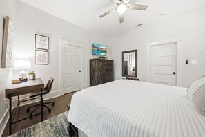 Une chambre à coucher comprenant un lit, un bureau, une chaise, une armoire et un ventilateur de plafond.