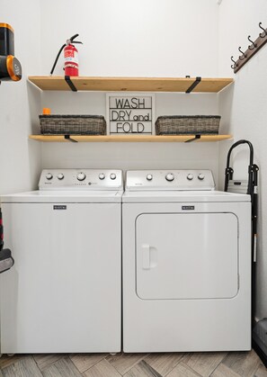 A laundry area with two Maytag washers and dryers, a sign above the dryers instructing to 'WASH DRY and FOLD,' and a fire extinguisher on the wall. - Escape to Gorman Grove—your private Waco sanctuary just 10 mins from Magnolia. <br>Whether you're gathering with family, friends or chasing Chip & Jo dreams, Gorman Grove has historic charm with modern comfort.  Welcome! (Waco)